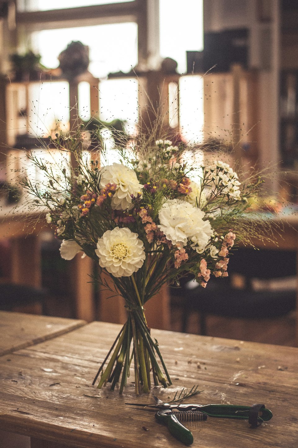 Vita dahlior och blomsterverktyg på ett rustikt träbord.