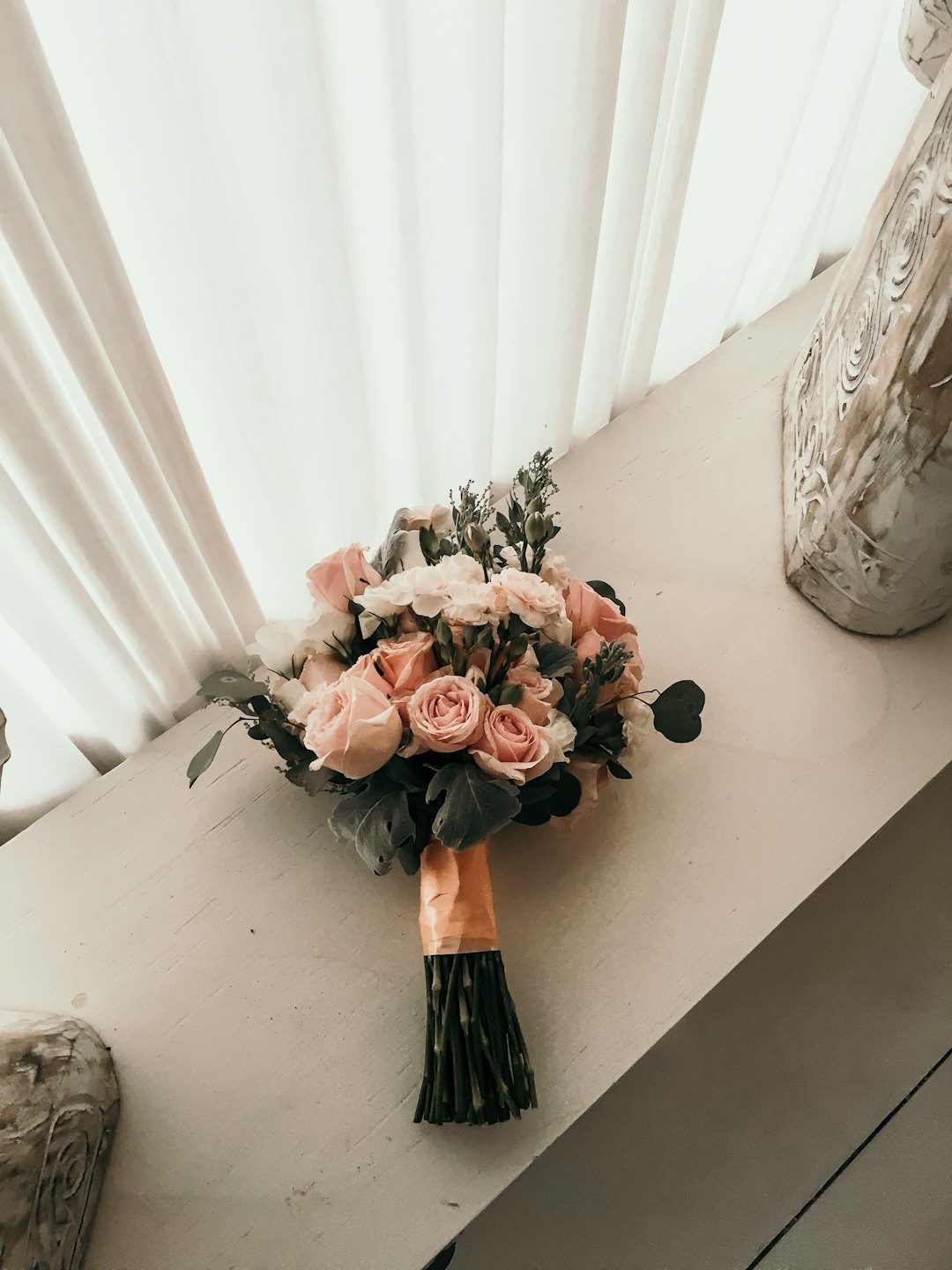Rosa och vita rosor med eukalyptus i en brudbukett på en trähylla.