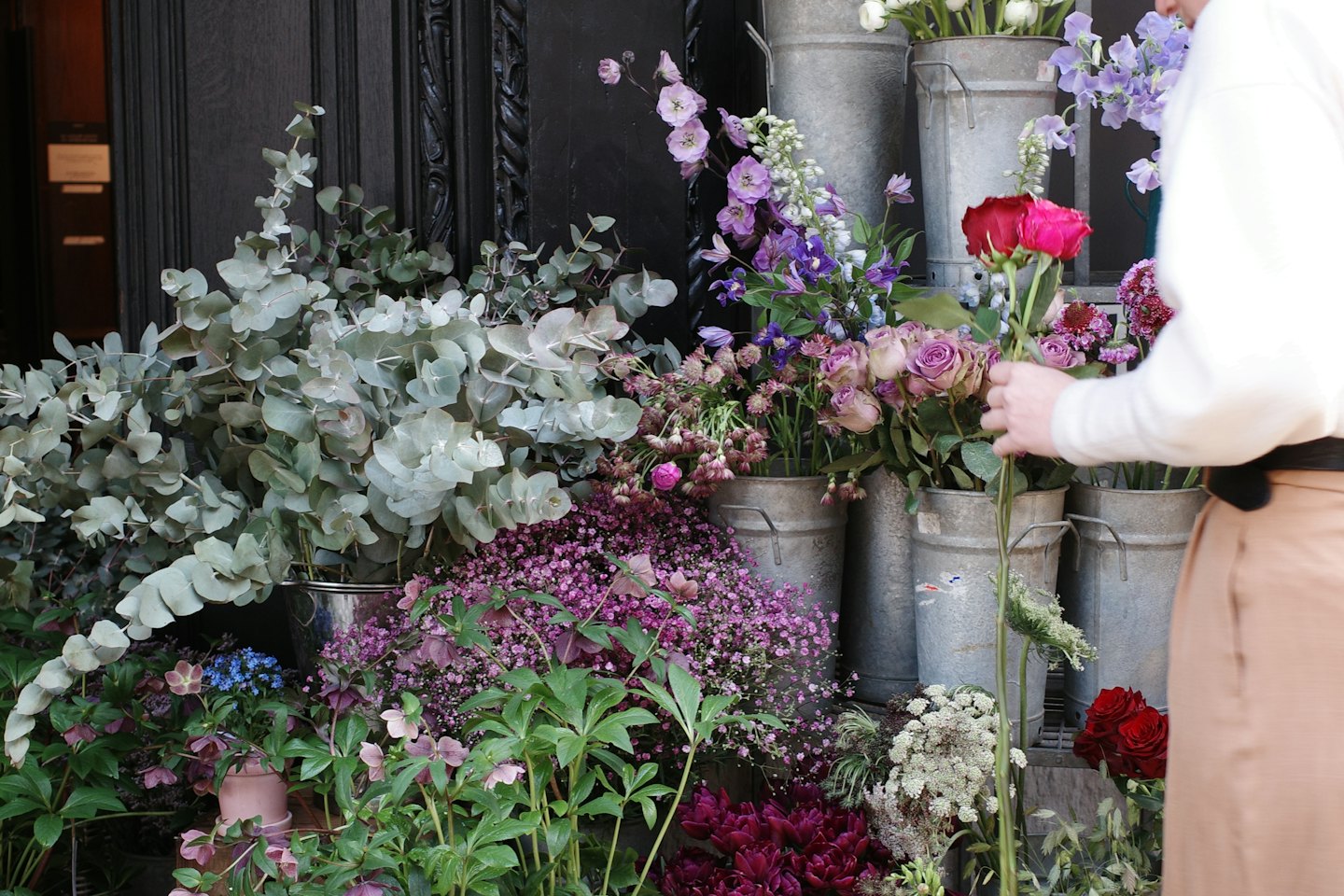 Florist som arrangerar färgglada blommor i hinkar utanför en butik.