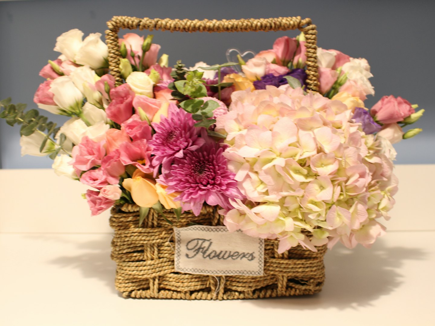 Rosa, vita och gula blommor arrangerade i en korg av flätat material.